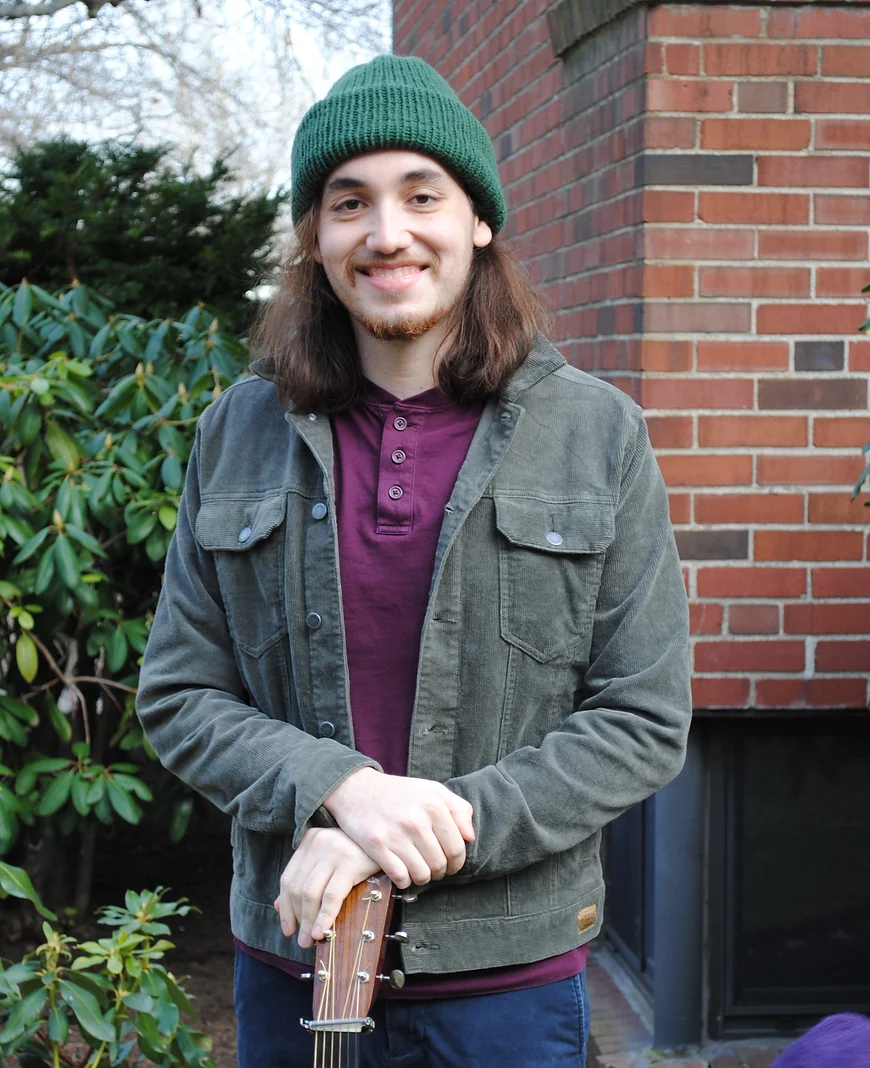 Caleb standing, smiling with a guitar